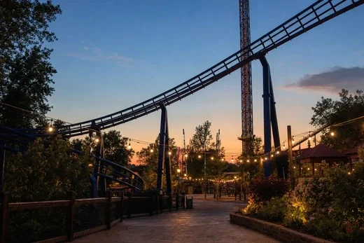 A rollercoaster track above a theme park walkway at dusk (AI-generated image)